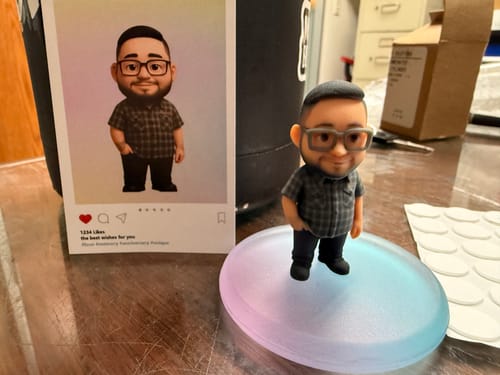 Customer's Custom Mini Me Figurine on a desk, placed next to the card with the reference image it's based on.