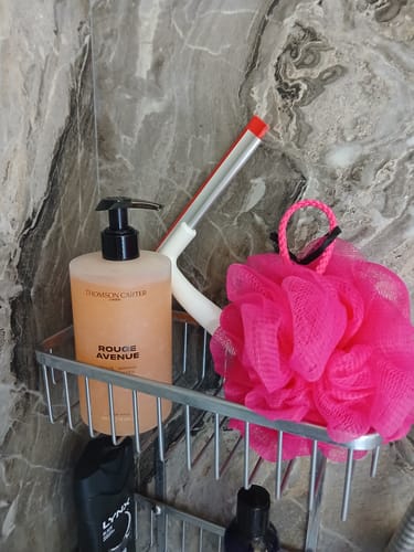 Customer's Rouge Avenue Body Wash in a silver shower caddy next to a bright pink loofah against a marble wall.