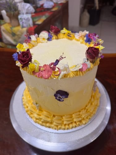 Customer's yellow frosted cake decorated with a ring of colorful FUCHSIA freeze dried edible flowers.