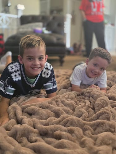Reviewer's two children smiling while lying on the large, soft Biggest Hugs Milk Chocolate Blanket.
