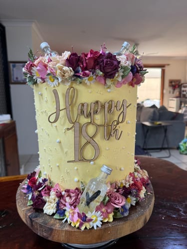 Customer's yellow 18th birthday cake adorned with freeze-dried white daisies and other colorful flowers.