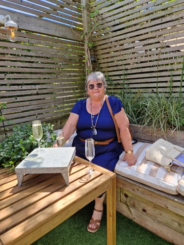 Customer in a blue dress relaxing on an outdoor patio with a drink.
