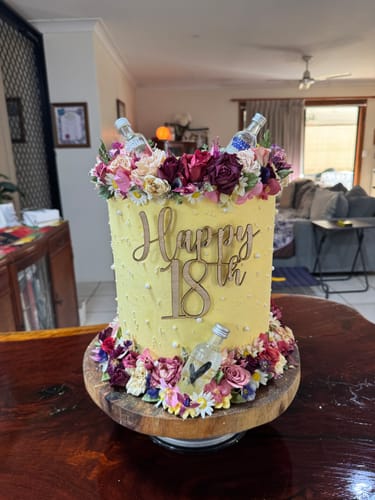 Customer's tall birthday cake decorated with colorful flowers from the Bespoke Bloomish Box on the top and base.