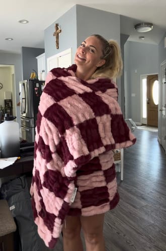 Reviewer smiling while wrapped cozily in the plush Hugs Devin Pink Checkered Blanket.