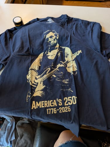 Reviewer's dark blue Lincoln 250 T-Shirt laid out, showing the graphic of Lincoln playing guitar.