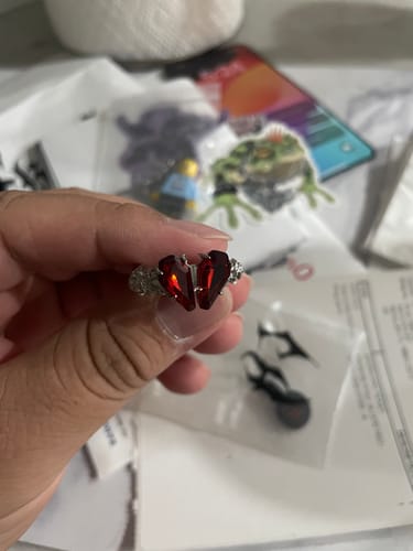 Reviewer holding a silver-colored ring with a red, split-heart stone.