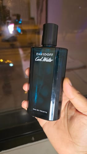 عميل يمسك بزجاجة عطر دافيدوف كول ووتر الزرقاء.