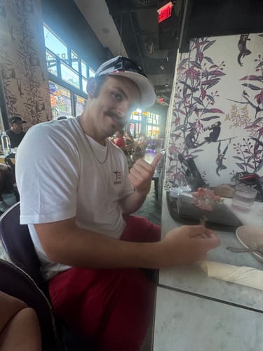 Reviewer wearing the white 250th Anniversary Tee, giving a thumbs-up while seated at a table.