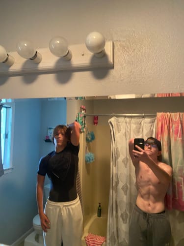 Customer poses in a bathroom mirror wearing the fitted, black Superman Compression Tee.