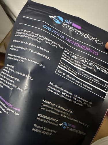 Un cliente sostiene el empaque negro de Creatina Monohidrato, mostrando la información que confirma que no tiene colorantes.