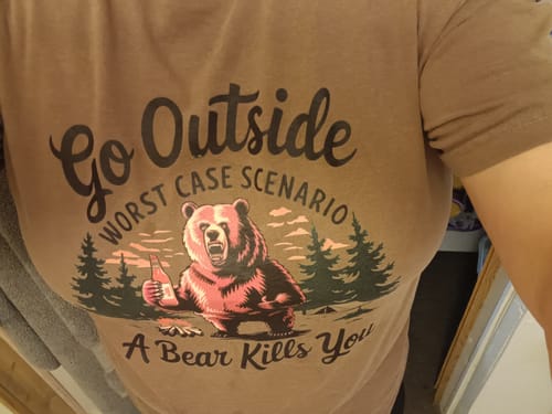 Customer wearing the brown Go Outside T-shirt with the humorous 'Worst Case Scenario' bear graphic.