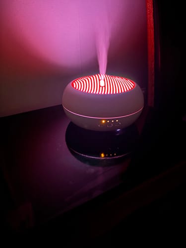 Recensent's Sakura aroma diffuser in een donkere kamer, die mist uitstoot terwijl hij roze oplicht.