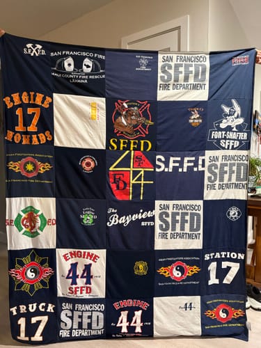 Customer holding up their custom Project Repat T-Shirt Quilt made from San Francisco Fire Department shirts.
