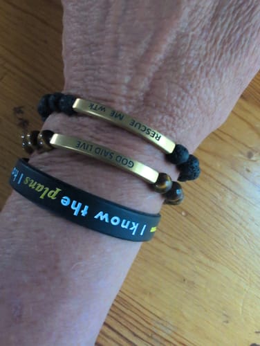 Customer's wrist wearing two beaded bracelets with engraved gold-tone plates and a black silicone bracelet.