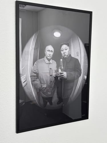 Customer's The Good Stuff art print of Putin and Kim Jong-un, shown in a thin black frame on a wall.