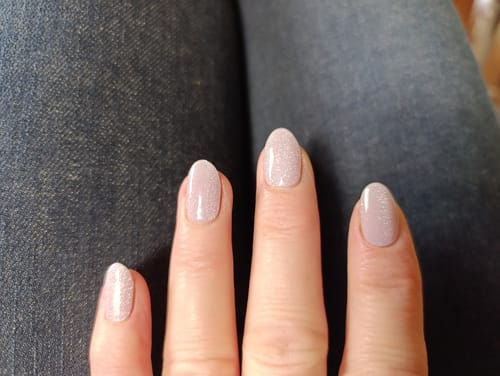 Nahaufnahme der Hand einer Kundin mit den schimmernden Glazed Donut Cateye UV-Gel-Nagelfolien auf mandelförmigen Nägeln.