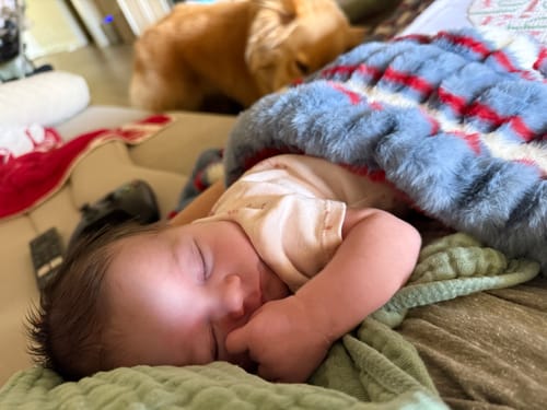 Customer's newborn sleeping under the soft Hugs Patriotic Stripe Blanket on a couch.