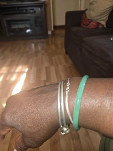A customer's wrist wearing the green AMALI Bangle alongside other silver bracelets.