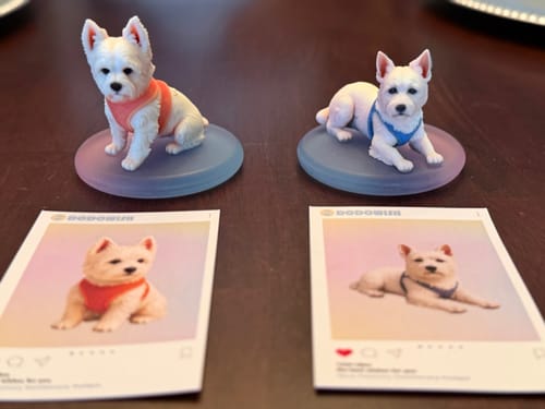 Reviewer's two custom 3D figurines of white dogs, one sitting with a red harness and one lying down with a blue harness.