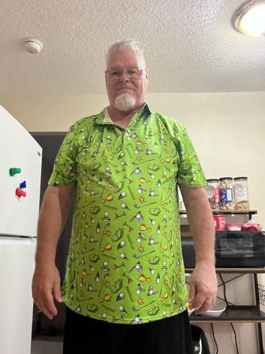 Reviewer standing indoors wearing the bright green printed Stadium Champion Men's golf polo.