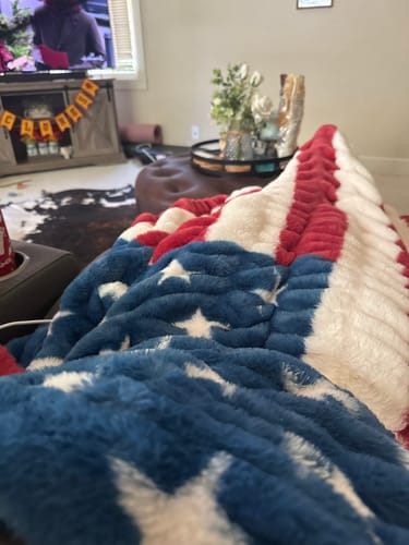 Customer relaxing on a couch under their plush Hugs Flag Blanket, showing a close-up of the texture.