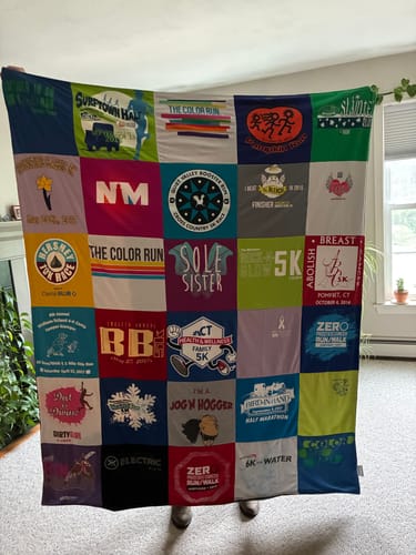 Customer holding up their colorful Project Repat T-Shirt Quilt made from a grid of various race t-shirts.