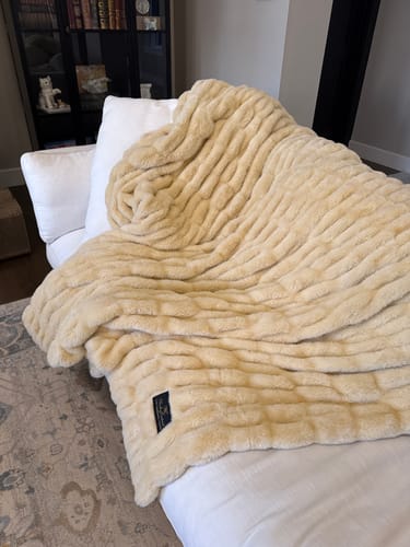 Customer's plush, monster-size Hugs Honey Butter Blanket draped across a white chaise lounge.