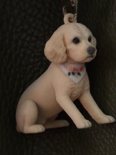 Customer's Identity Image keychain, a seated cream-colored puppy figurine with a floral bandana, against a dark background.