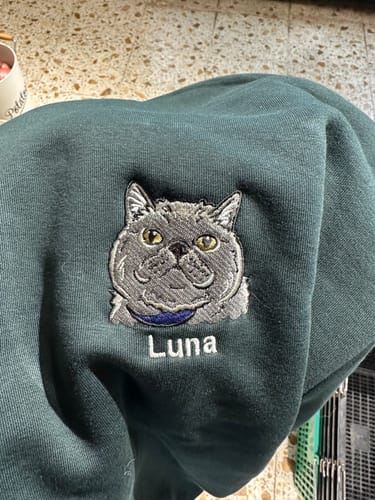 Close-up of a customer's dark green pet crew showing detailed embroidery of a grey cat named Luna.