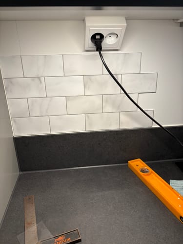 Anmelder som monterer de selvklebende Subway-marmorflisene på en kjøkkenvegg.