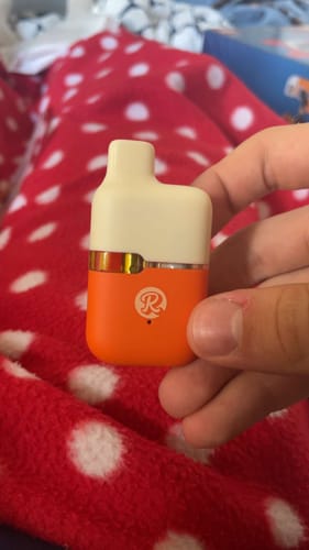 Customer holding the compact orange and cream 1ML THCA Vape in their hand against a polka-dot background.