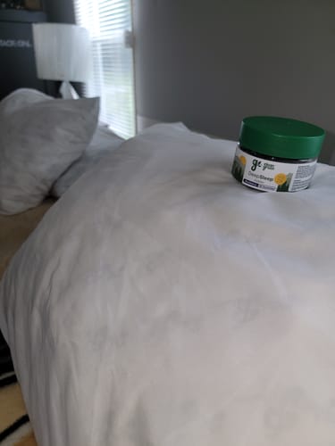 Customer's jar of DeepSleep Gummies with a green lid resting on a white pillow on a bed.