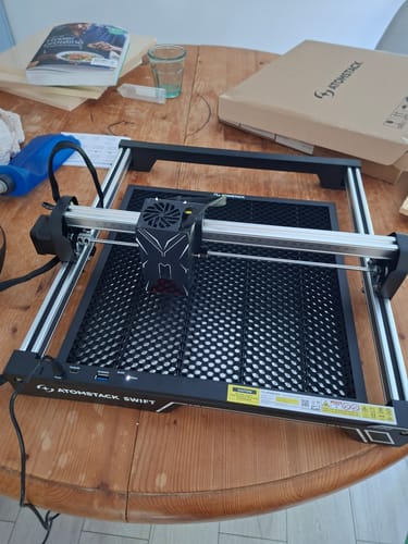 Reviewer's assembled AtomStack Swift Laser Engraver sitting on a wooden table with its packaging behind it.
