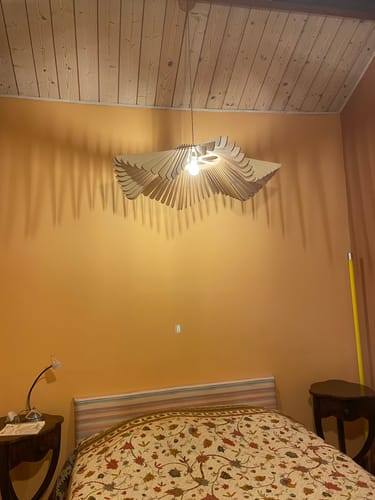 Avis d'un client : la suspension Rose allumée dans une chambre, projetant un motif d'ombres sur un mur orange.