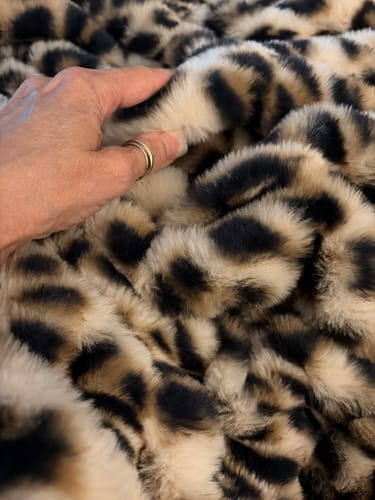 Close-up of a reviewer's hand feeling the soft, plush Hugs Golden Leopard Blanket.