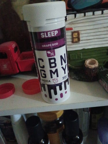 Customer's container of Grape God CBN Sleep Gummies sitting on a shelf among other items.