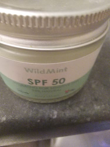 Customer's close-up of the SPF 50 jar with a silver lid on a dark counter.