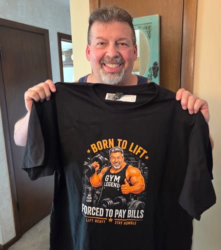 A smiling reviewer holds up his custom black Funny Gym Dad Graphic T-shirt with a personalized caricature.