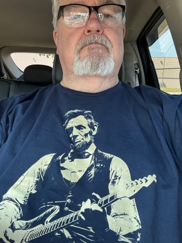 Reviewer wearing the navy blue Lincoln 250 T-Shirt with a graphic of Abraham Lincoln playing an electric guitar.