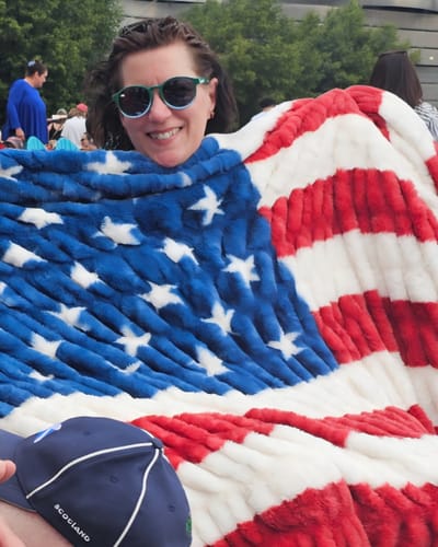 Reviewer smiling while wrapped in the plush Hugs Flag Blanket at an outdoor movie.