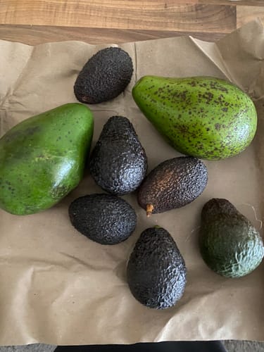 Ein Kunde zeigt die verschiedenen Avocados aus der Mix-Box, die auf braunem Packpapier liegen.