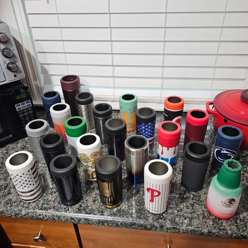 Customer's large collection of varied Frost Buddy can coolers displayed on a kitchen counter.