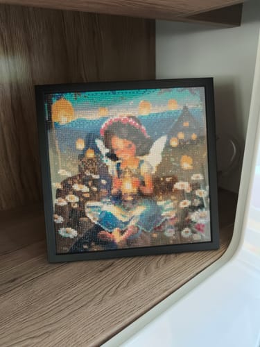 Das fertige Diamond Painting 'Fee auf dem Bauernhof' eines Kunden, in einem schwarzen Rahmen auf einem Regal.