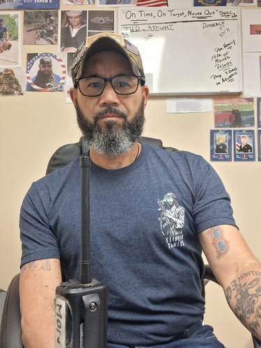 Reviewer sitting indoors wearing the blue Flippin' Tables T-Shirt, showing its athletic fit and chest graphic.