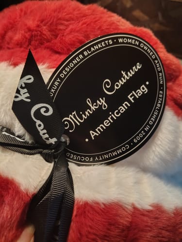 Close-up of a reviewer's Hugs Flag Blanket, showing its soft, plush material and attached 'Minky Couture' brand tag.