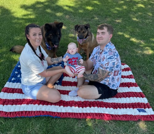 Reviewer's family sitting with a baby and two dogs on the plush Hugs Flag Blanket in a grassy area.