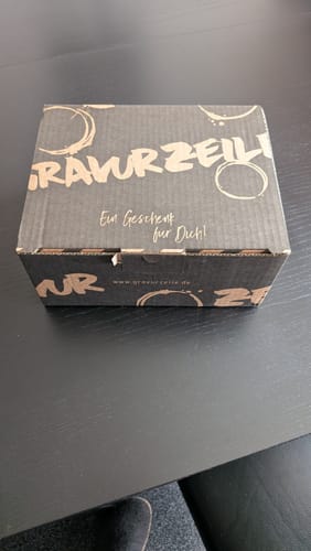 Rezensent zeigt die stabile Geschenkverpackung von Gravurzeile auf einem Tisch.