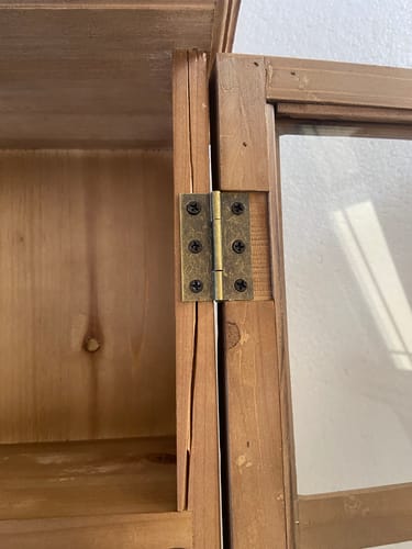 Customer's close-up of the Alain Wall Cabinet showing a large crack in the pine wood next to the door hinge.