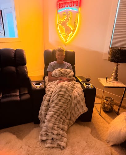 Customer relaxing in a recliner, wrapped in a plush, tan Hugs Topaz blanket.