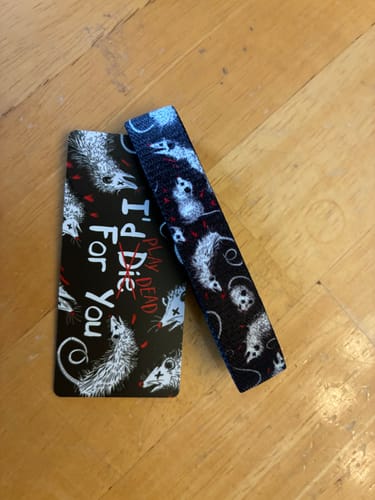 Reviewer's 'I'd Play Dead For You' Bracelet and matching card with a possum pattern on a wooden surface.